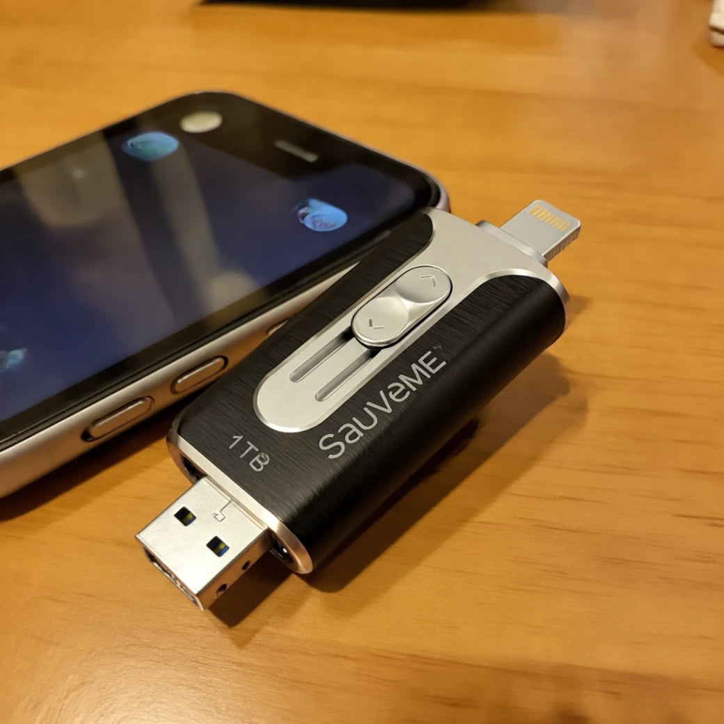 Clé USB de sauvegarde SauveMe 1 To posée à côté d'un iPhone sur une table en bois, montrant le connecteur Lightning